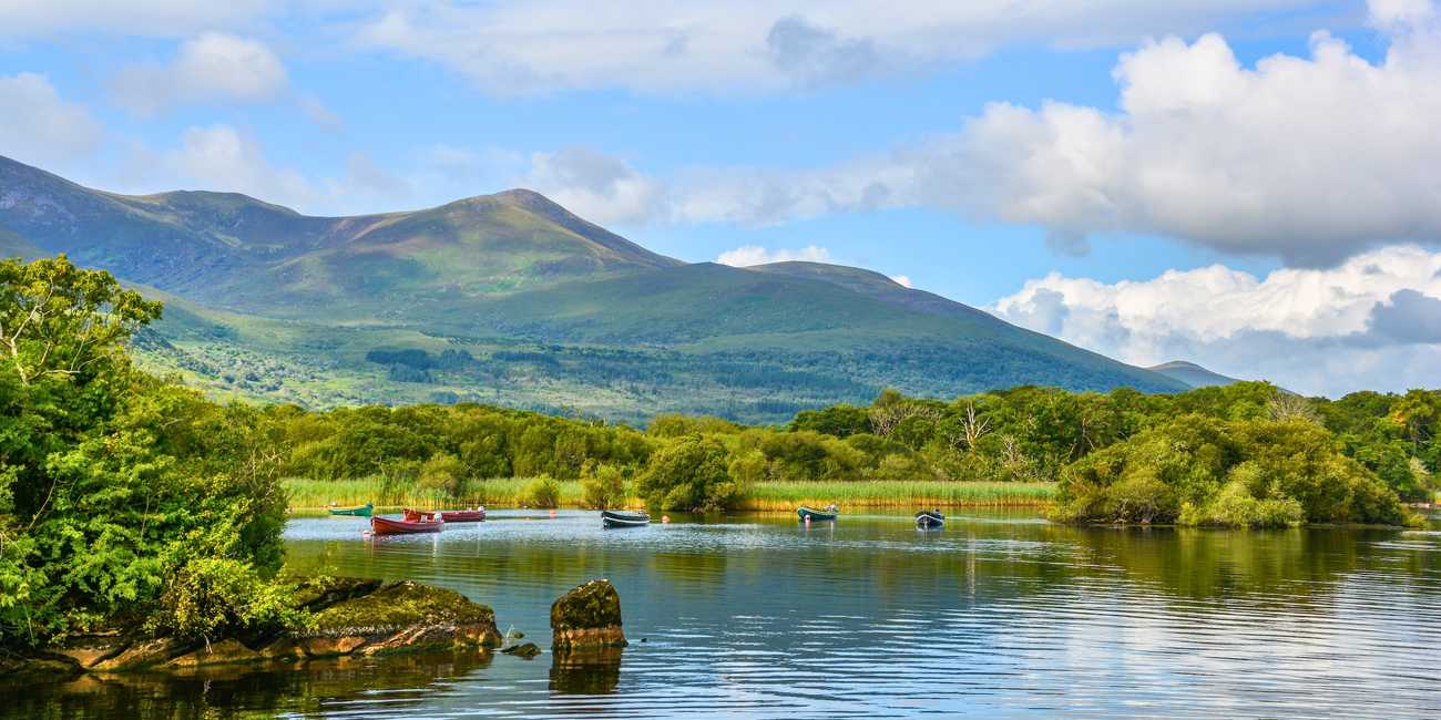 Absorb Ireland's natural beauty – Compare premium Ring of Kerry day trips and local national park excursions online for 2026 Traditional wooden fishing boats floating peacefully on the glassy waters of the Lakes of Killarney beneath the sweeping green mountain peaks of County Kerry in 2026